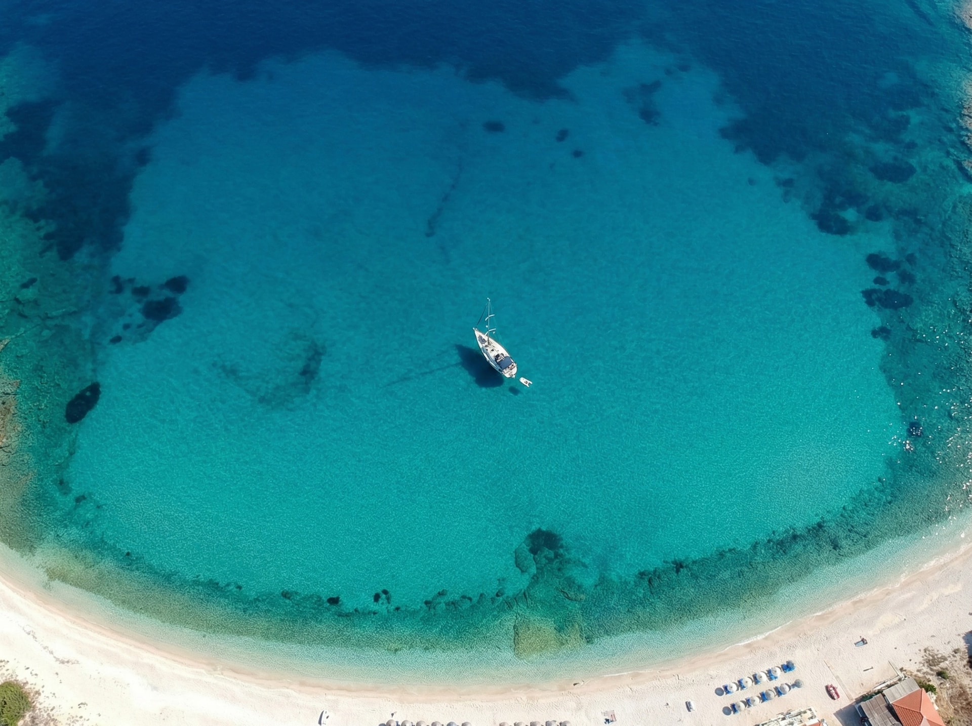 Aerial view of a sailing boat anchored in crystal clear turquoise waters near a sandy beach in Greece